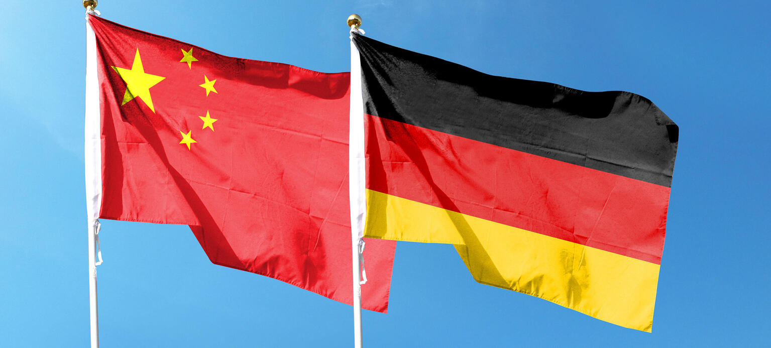 Chinesische Flagge und die deutsche Flagge wehen an einem Mast im blauen Himmel.
